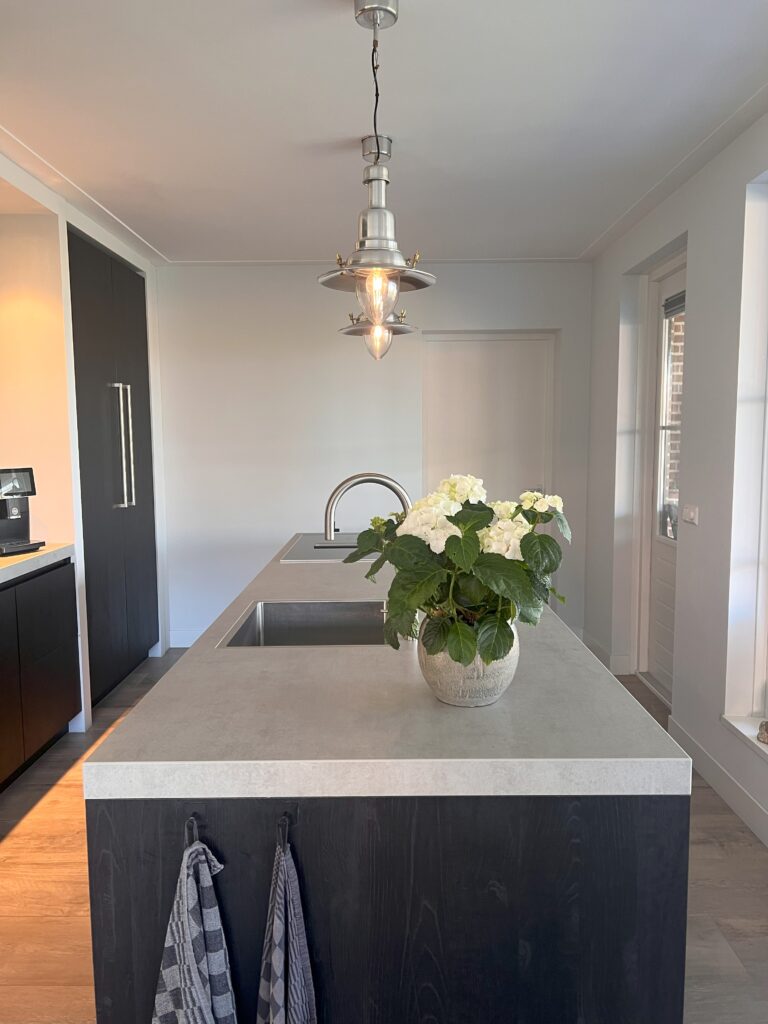 Licht beton look blad gemaakt van composiet met zwarten houten kasten eronder en een plant op het aanrechtblad