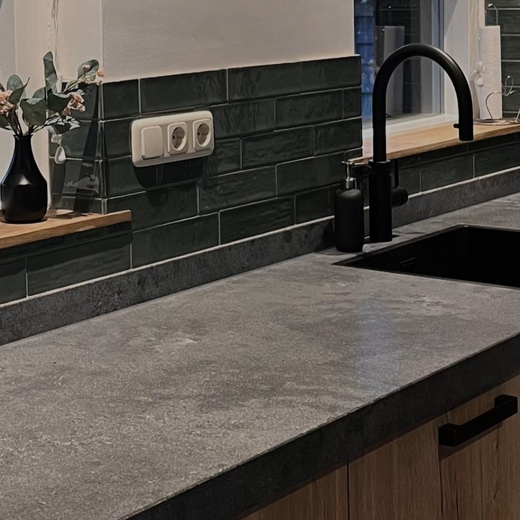 Donker composiet aanrechtblad met aansluitende plint tegen de muur aan en een gunmetal kraan en spoelbak.